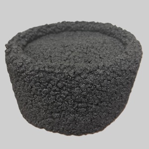 May include: A black, cylindrical hat with a textured, fuzzy surface. The hat has a rounded top and a slightly wider brim. The hat appears to be made of a thick, dark material, possibly wool or a similar fabric. The hat is a solid color and has a simple, classic design.