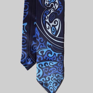 Könnte beinhalten: Eine marineblaue Krawatte mit einem sich wiederholenden Muster aus stilisierten blauen und weißen Stammesdesigns. Die Krawatte hat ein spitzes Ende und besteht aus einem glatten Material. Das Design ist aufwendig und detailliert.