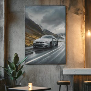 May include: A framed print of a silver sports car driving on a wet road through a mountain landscape. The car is the focal point, with the road and mountains in the background. The print is displayed on a textured gray wall.