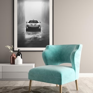 Puede incluir: Una fotografía en blanco y negro de un coche deportivo en un túnel está enmarcada sobre un sillón turquesa con patas de madera. La habitación también cuenta con un mueble blanco con jarrones y una alfombra estampada.