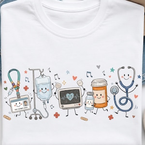 May include: A white t-shirt featuring a colourful graphic print of anthropomorphic medical items including an ID badge, an IV bag, a heart monitor, a medicine bottle, and a stethoscope, all with smiling faces, surrounded by small stars and hearts.