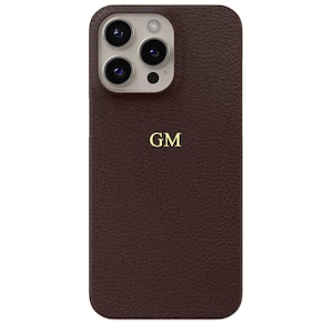 Könnte beinhalten: Eine braune Leder-Handyhülle mit einem goldenen Monogramm "GM" auf der Rückseite. Die Hülle hat einen Kameraausschnitt für ein Dreifach-Objektivsystem.