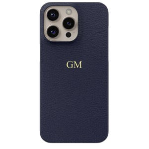 Puede incluir: Una funda de teléfono de cuero azul marino con un acabado texturizado. La funda presenta un monograma dorado con las letras "GM" y un recorte para la cámara. La funda está diseñada para proteger el teléfono.