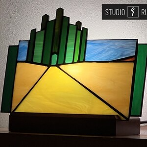 May include: A stained glass lamp depicting the yellow brick road leading to the Emerald City from the Wizard of Oz. The lamp features a green cityscape with a yellow brick road leading to a bright yellow center.
