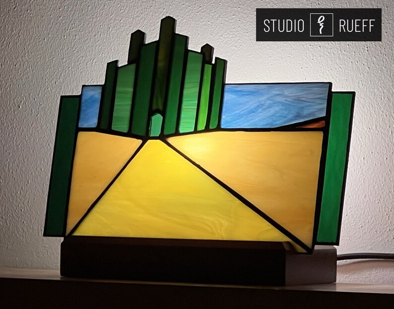 May include: A stained glass lamp depicting the yellow brick road leading to the Emerald City from the Wizard of Oz. The lamp features a green cityscape with a yellow brick road leading to a bright yellow center.