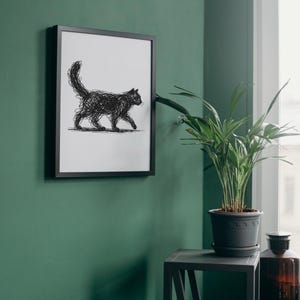 May include: Black framed art print showing a scribble-style illustration of a cat walking. The artwork is on a white background, mounted on a dark green wall. A potted plant sits on a small table nearby.