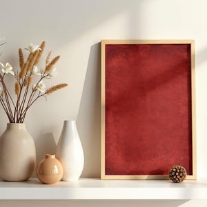 Puede incluir: Una obra de arte roja enmarcada con un marco de madera se encuentra en un estante blanco junto a tres jarrones de cerámica y una pequeña piña decorativa. Los jarrones son de color beige, blanco y melocotón.