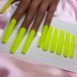 Op de afbeelding: Een set van tien neon gele press-on nagels met een glitter finish. De nagels zijn lang en in een kistvorm.