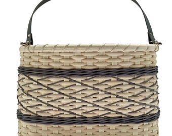 May include: A rectangular woven basket handbag featuring a light beige natural reed body with a contrasting dark brown woven band across the center. The bag includes a single dark brown arched handle attached with silver-toned metal hardware.