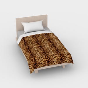 May include: A twin-sized bed with a brown and black leopard print duvet cover and a white pillow. The bed frame is made of wood and has a light brown finish.
