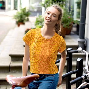 May include: A woman wearing a yellow and orange leopard print cropped t-shirt with short sleeves. She is standing in front of a bicycle rack.