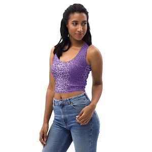 May include: A purple crop top with a leopard print pattern. The top has a scoop neck and is sleeveless. The fabric is a soft, stretchy material. The top is worn with blue jeans.