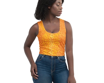 May include: A sleeveless crop top with a scoop neckline. The top features a vibrant orange and yellow leopard print pattern. The model is wearing blue jeans.