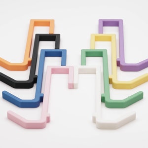 May include: A collection of colorful, plastic over-the-door hooks in various shades, including orange, black, blue, pink, white, green, yellow, and purple. These hooks are designed to hang over a door and provide additional storage.