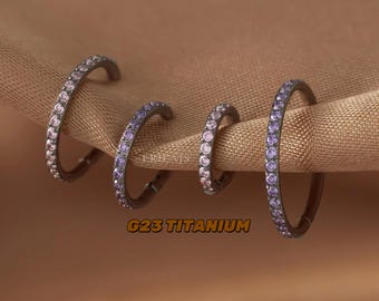 Peut inclure: Trois boucles d'oreilles créoles noires avec un dégradé de pierres précieuses violettes et roses. Les boucles d'oreilles sont en titane G23.