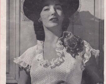 May include: A woman wearing a white crocheted top with a ruffled neckline and short sleeves. She is wearing a black hat with a veil and a large flower brooch.