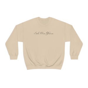May include: A beige sweatshirt with the text "Soli Deo Gloria" printed in black on the front.