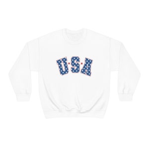 May include: White crew neck sweatshirt with the word "USA" in blue letters filled with white stars. The letters are outlined in red. A casual, patriotic apparel item.
