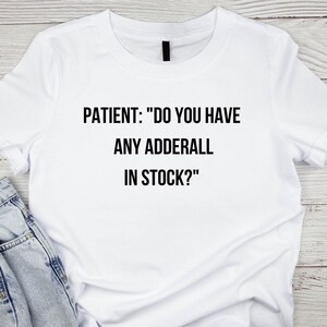 May include: White t-shirt with black text that reads "PATIENT: "DO YOU HAVE ANY ADDERALL IN STOCK?"