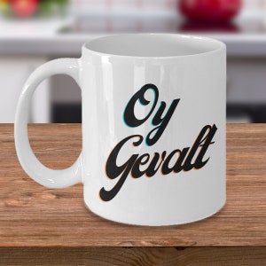 May include: White ceramic coffee mug with a black and orange design that says "Oy Gevalt" in a stylized font.