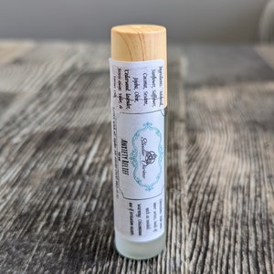 May include: A clear glass roller bottle with a wooden cap and a white label that reads "Studio Divine Anxiety Relief 10 ml". The label also lists the ingredients and directions for use.