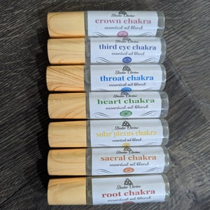 May include: Seven wooden roller bottles with labels for different chakra essential oil blends. The labels are white with black text and a colorful chakra symbol. The labels read: crown chakra, third eye chakra, throat chakra, heart chakra, solar plexus chakra, sacral chakra, and root chakra.