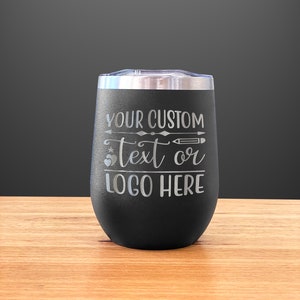 May include: Black stainless steel wine tumbler with a silver engraved design that says "YOUR CUSTOM text or LOGO HERE" with a star, heart, and pencil graphic.