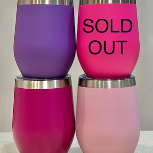 Puede incluir: Cuatro vasos de vino de acero inoxidable. Dos son rosas, uno es morado y uno es rosa claro. El vaso rosa del centro tiene el texto "SOLD OUT" impreso.