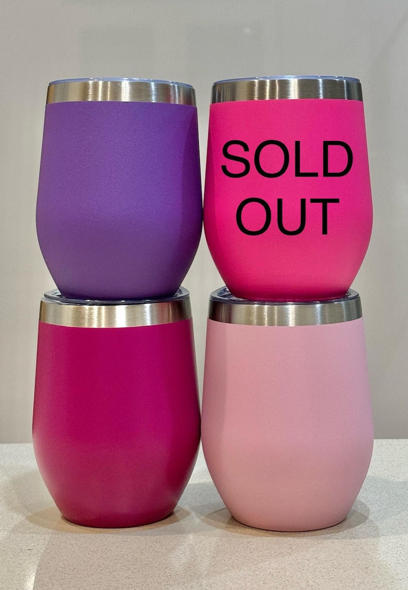 Puede incluir: Cuatro vasos de vino de acero inoxidable. Dos son rosas, uno es morado y uno es rosa claro. El vaso rosa del centro tiene el texto "SOLD OUT" impreso.