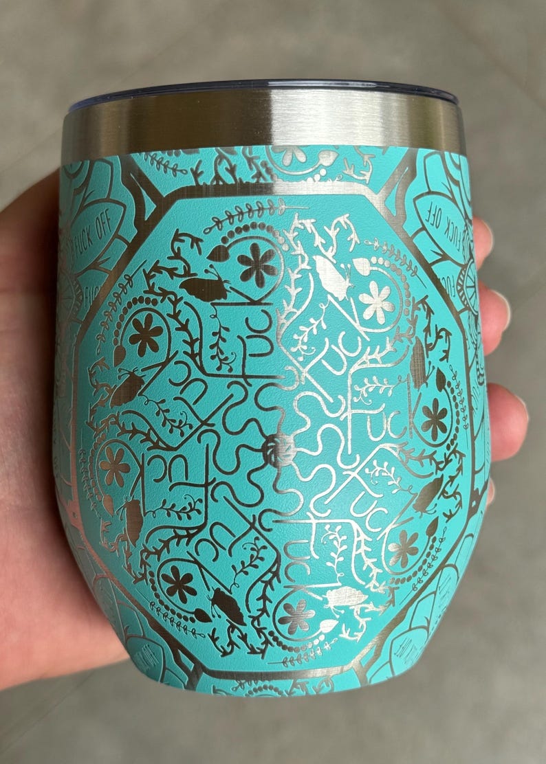 Puede incluir: Un vaso de acero inoxidable turquesa con un dise&ntilde;o met&aacute;lico plateado que presenta un patr&oacute;n repetitivo de flores, hojas e insectos. El texto "F*CK OFF" es visible en el lateral del vaso.