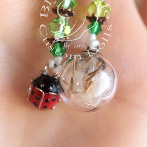 May include: A green crystal beaded necklace with a copper charm and a glass orb containing a dandelion seed. A ladybug charm is attached to the orb.