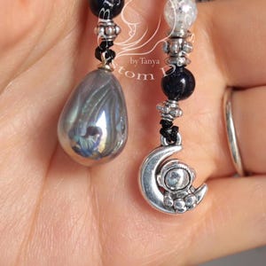 May include: A black and silver beaded necklace with a silver crescent moon charm and a iridescent teardrop pendant.