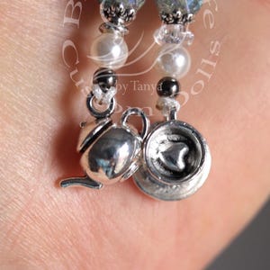 May include: A pair of silver charm bracelets with a teapot and teacup charm. The bracelets are made with white pearls, clear crystals, and iridescent green beads.