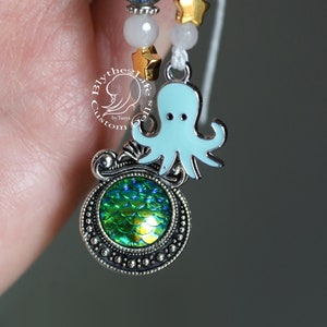 May include: A silver charm bracelet with a green mermaid scale charm, a blue octopus charm, and white and blue beads.