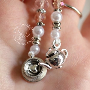 May include: A silver charm necklace featuring a teapot and teacup charm. The necklace is made with white and pink beads.