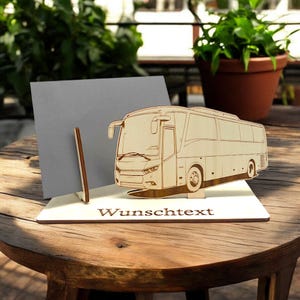 Könnte beinhalten: Ein detailliertes Busmodell aus Holz, das auf einer weißen Basis steht. Auf der Basis steht das Wort "Wunschtext". Hinter dem Bus ist eine graue Karte aufgestellt. Der Bus hat eine helle braune Farbe.