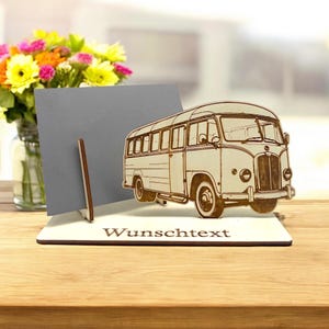 Könnte beinhalten: Ein Holz-Kartenhalter mit einem Ausschnitt eines Oldtimer-Busses. Der Kartenhalter hat eine graue Karte drin und der Text "Wunschtext" ist in die Basis graviert.