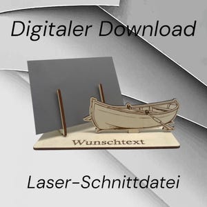 May include: A laser-cut wooden boat with oars, displayed on a wooden base with the text "Wunschtext". A gray card is propped up behind the boat. The text "Digitaler Download" and "Laser-Schnittdatei" are displayed above and below the boat.