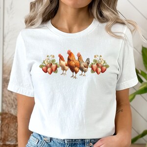 May include: White t-shirt with a graphic of four chickens and strawberries. The chickens are brown, white, and gray.
