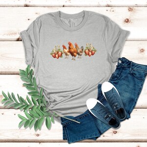 May include: A gray t-shirt with a design of three chickens and strawberries. The chickens are brown and white, and the strawberries are red.