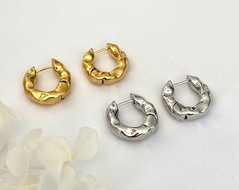 May include: Two pairs of hoop earrings, one pair is gold and the other is silver. Both pairs have a textured, irregular surface.
