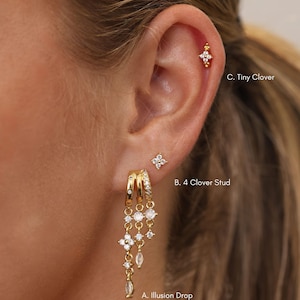 May include: Gold-toned jewellery set featuring three distinct pieces: A. Illusion Drop, a multi-chain dangle earring with clear stones; B. 4 Clover Stud, a small four-petaled flower earring; and C. Tiny Clover, a small floral stud earring.