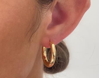 May include: A close-up of a gold hoop earring worn on an ear. The earring is a thick, rounded shape with a shiny, polished finish. The earring is a classic style, suitable for everyday wear.