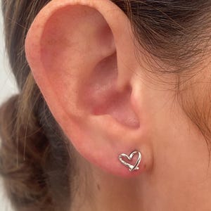 May include: A pair of silver heart-shaped stud earrings. The earrings are small and delicate, and they are perfect for everyday wear.