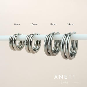 May include: Four silver hoop earrings in different sizes: 8mm, 10mm, 12mm, and 14mm. The earrings are stacked on a white surface. Anett Jewelry is printed below the earrings.