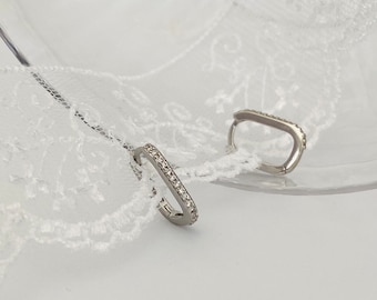 May include: A pair of silver hoop earrings with a row of clear cubic zirconia stones around the edge.