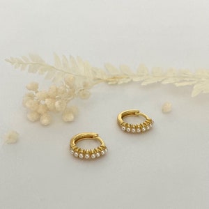 May include: A pair of gold hoop earrings with a row of small white pearls around the hoop.