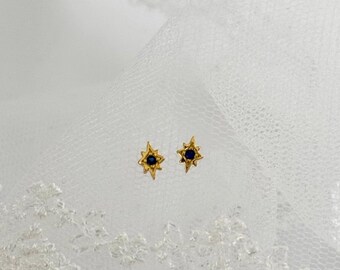 May include: A pair of gold star-shaped earrings with a small blue gemstone in the center of each star.