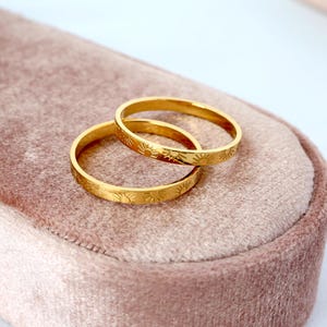 May include: Two gold-toned rings with a sun design engraved on the band. The rings are stacked on top of each other.