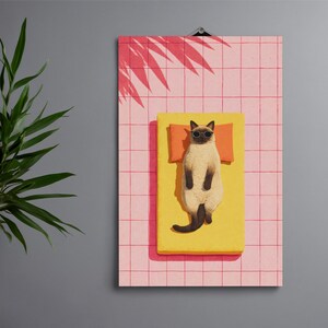 May include: A framed print featuring a lounging Siamese cat wearing sunglasses on a yellow sunbed with an orange pillow. The background is a pink grid pattern with a palm tree shadow.